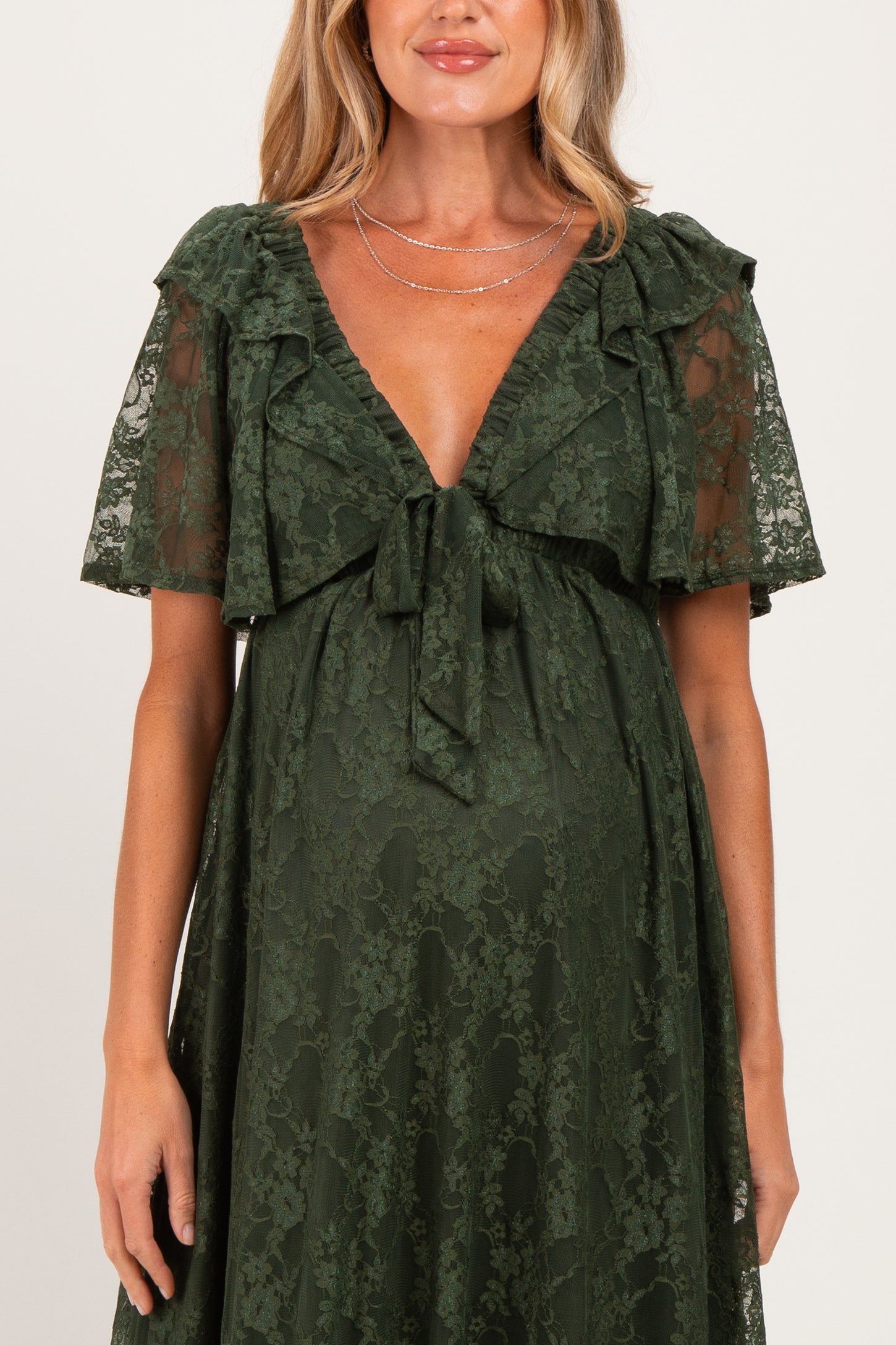 woman wearing a dark green lace maternity dress with short flutter sleeves and a tie detail at the chest, baby bump visible