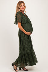 woman in a dark green lace maternity dress with flounced sleeves, holding her baby bump while posing sideways