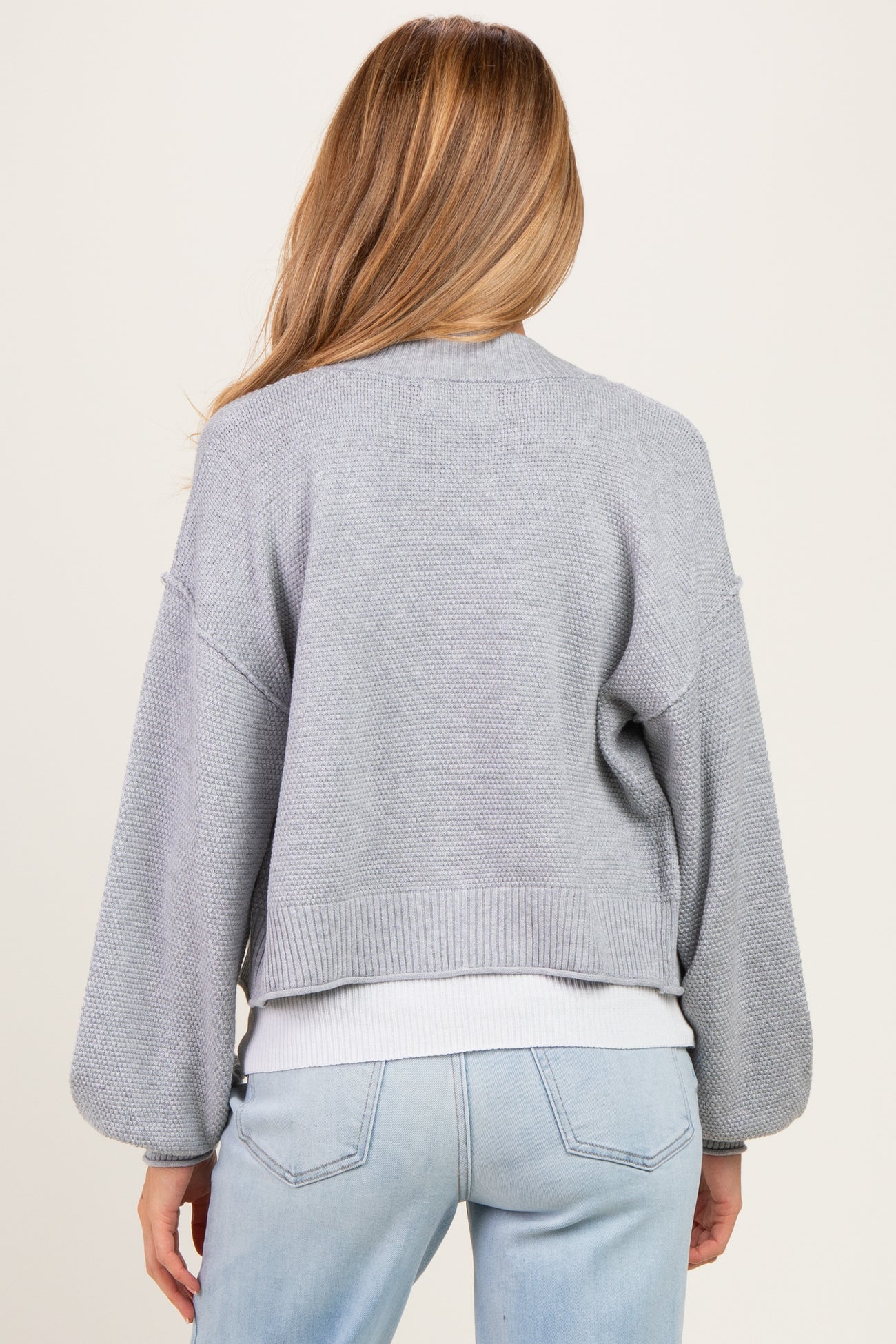 woman wearing a light gray cropped maternity cardigan with balloon sleeves, from the back