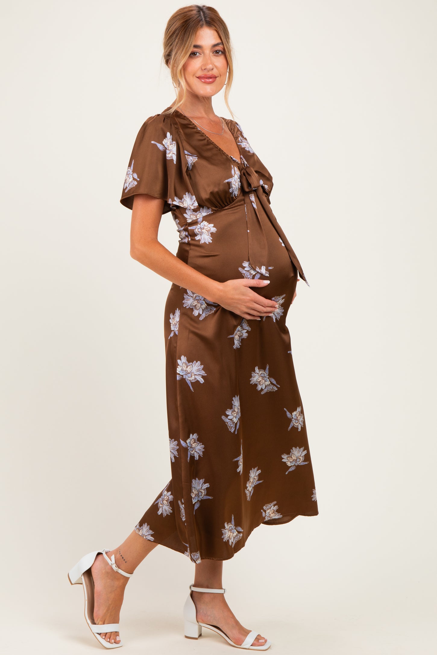 woman wearing a brown floral print maternity dress with a tie front and holding her baby bump