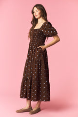 woman wearing a brown polka dot maxi dress with puff sleeves and smocked bodice, styled with side pockets