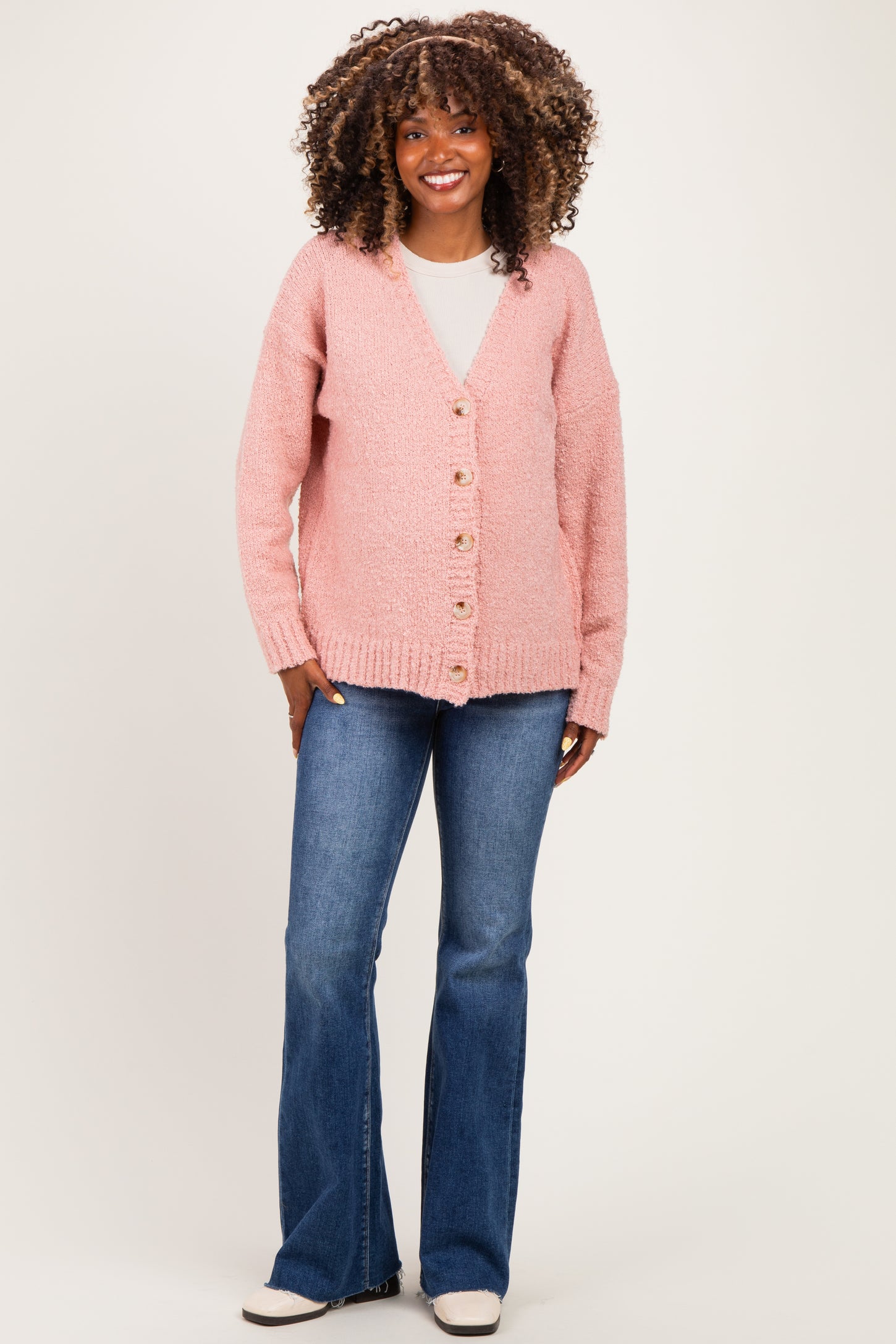 woman wearing a soft pink maternity cardigan with buttons, paired with blue flared jeans