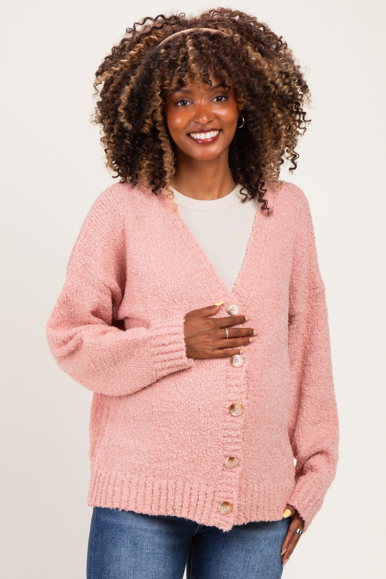 woman wearing a soft pink maternity cardigan with buttons, smiling and gently holding her baby bump