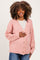 woman wearing a soft pink maternity cardigan with buttons, smiling and gently holding her baby bump