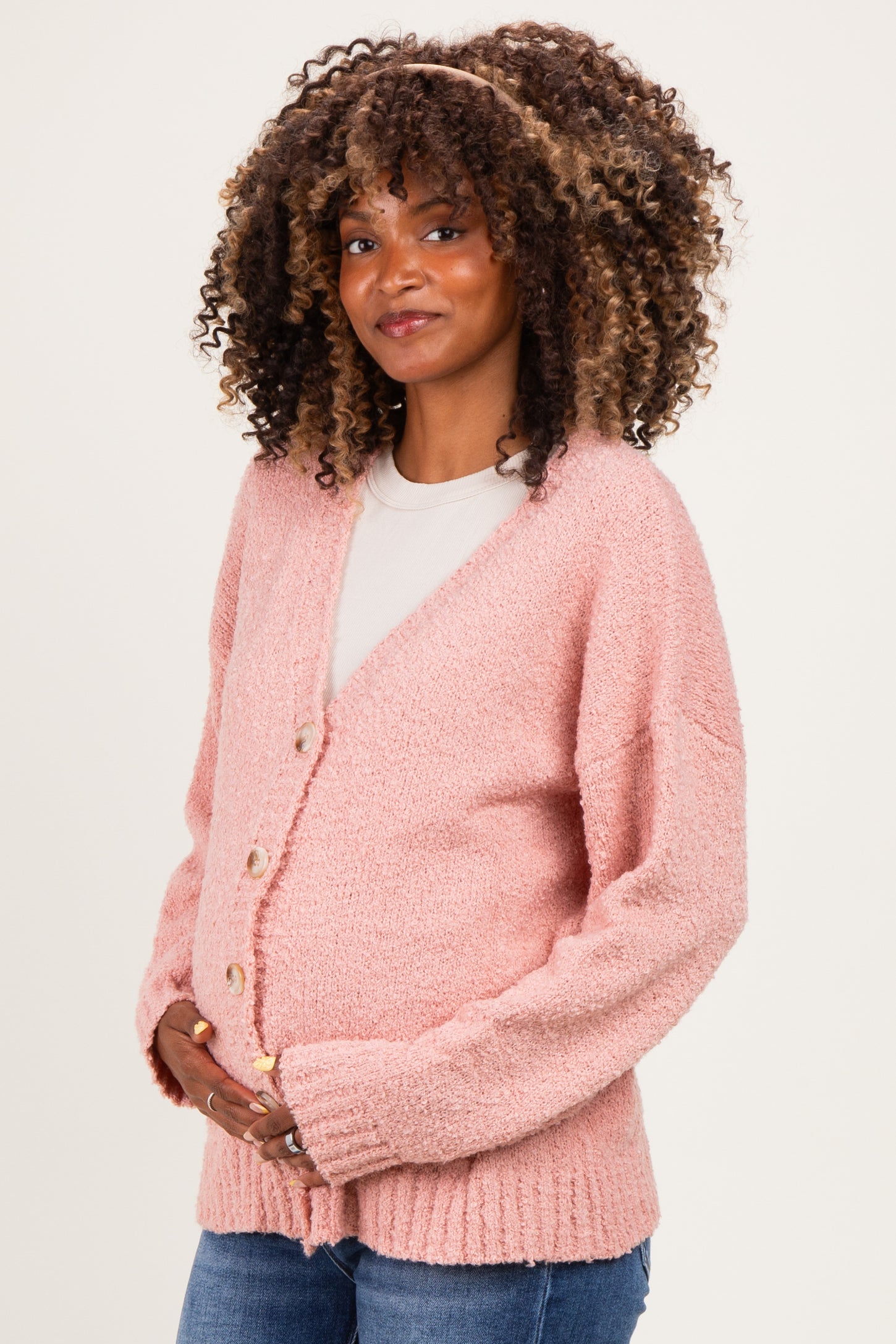 woman wearing a pink maternity cardigan with buttons and a visible baby bump, styled with jeans