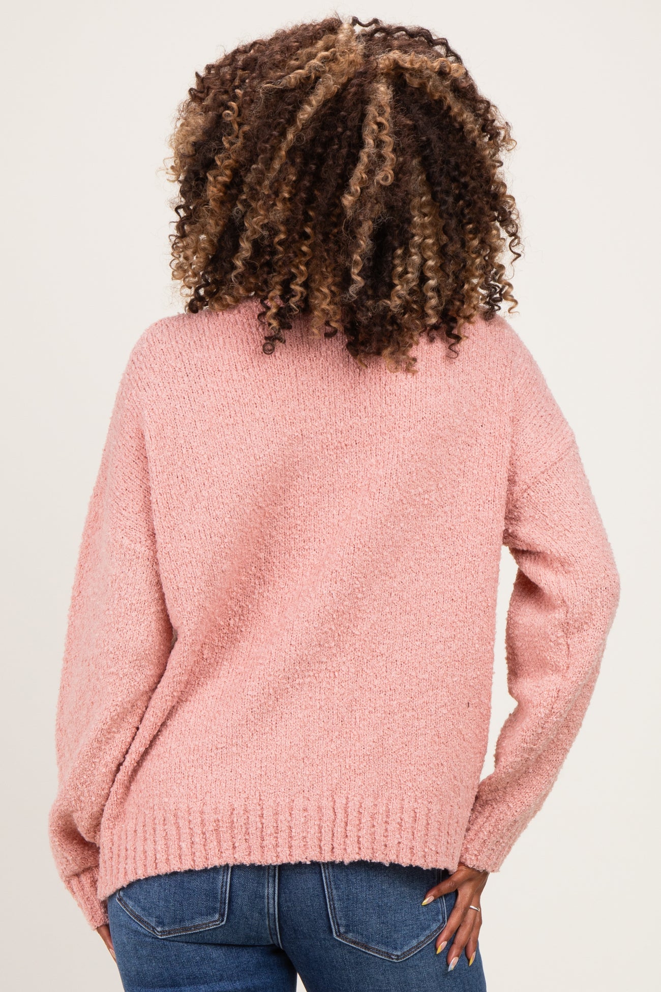 woman wearing a pink fuzzy maternity sweater, showing the back view, paired with blue jeans