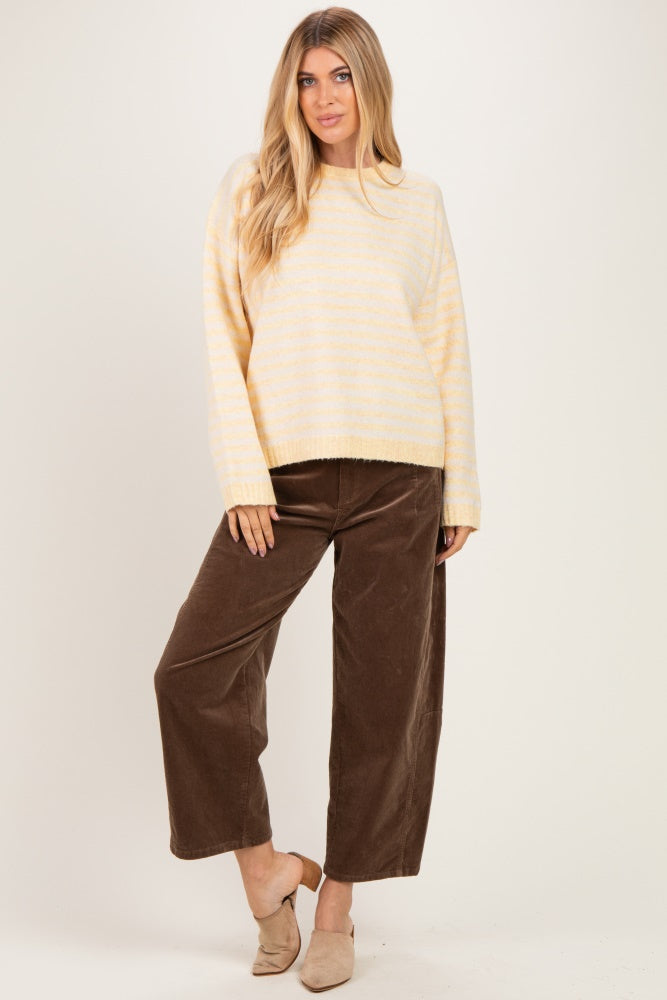 woman wearing a light yellow striped sweater and brown wide-leg corduroy pants, standing against a plain background