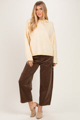 woman wearing a light yellow striped sweater and brown wide-leg corduroy pants, standing against a plain background