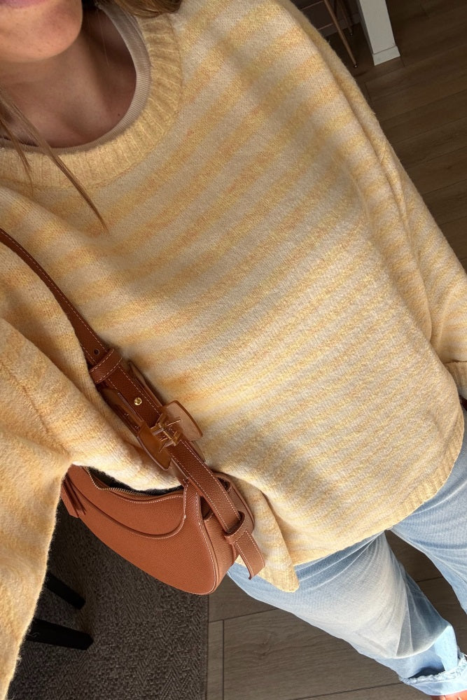 woman wearing a yellow striped oversized sweater with a relaxed fit and carrying a brown crossbody bag.