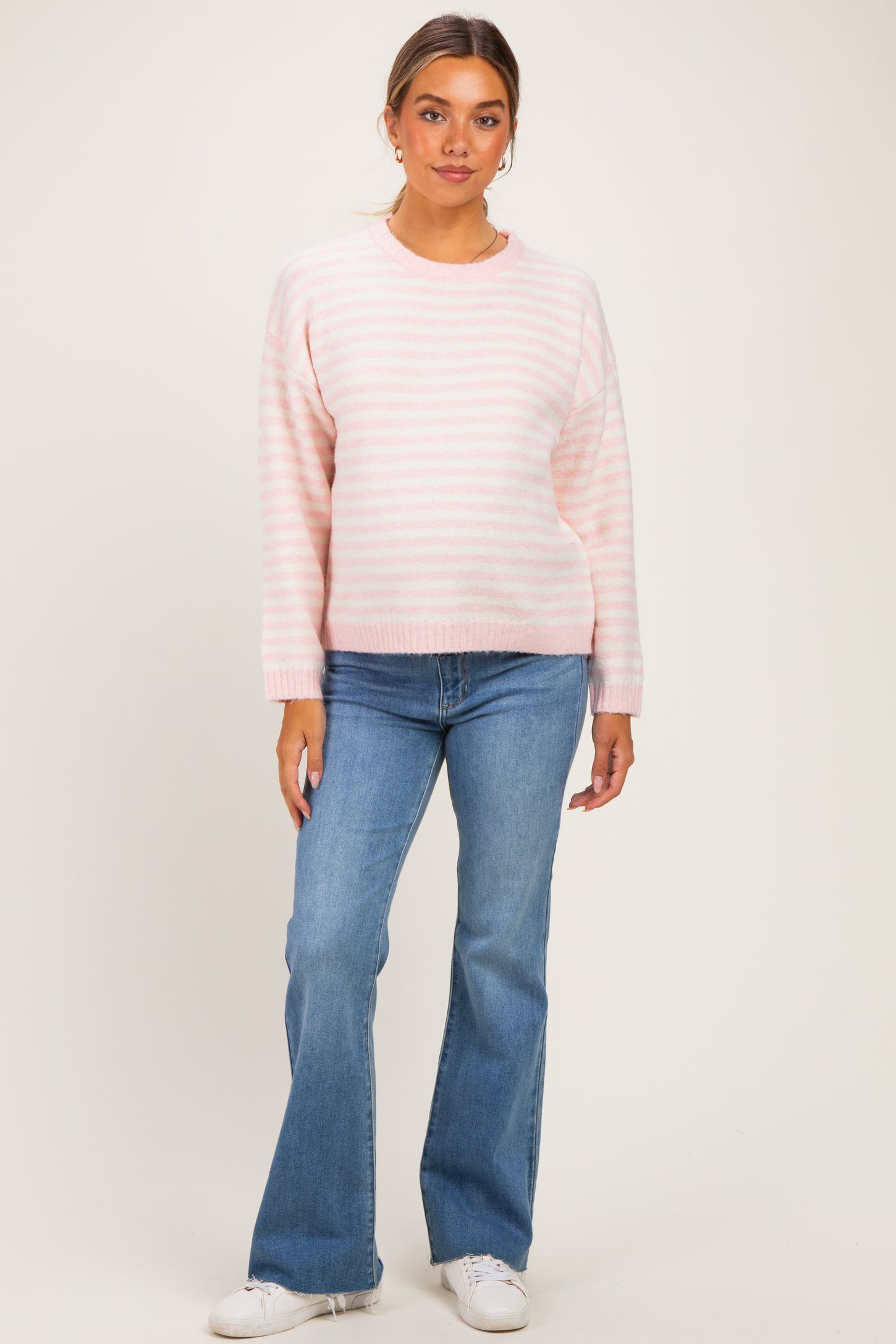 woman wearing a light pink striped maternity sweater and blue flared jeans, with a relaxed fit
