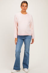 woman wearing a light pink striped maternity sweater and blue flared jeans, with a relaxed fit