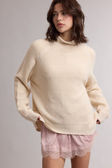 woman wearing a cream oversized sweater with a high neck and raglan sleeves, paired with pink lace-trimmed shorts