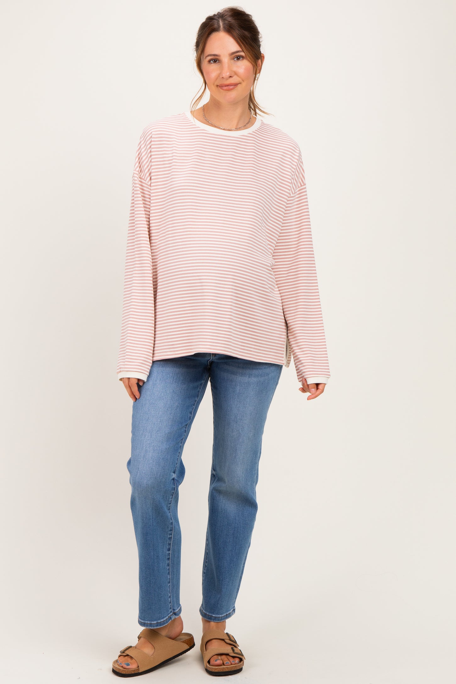 woman wearing a light pink and white striped maternity top with long sleeves and blue jeans, showing her baby bump