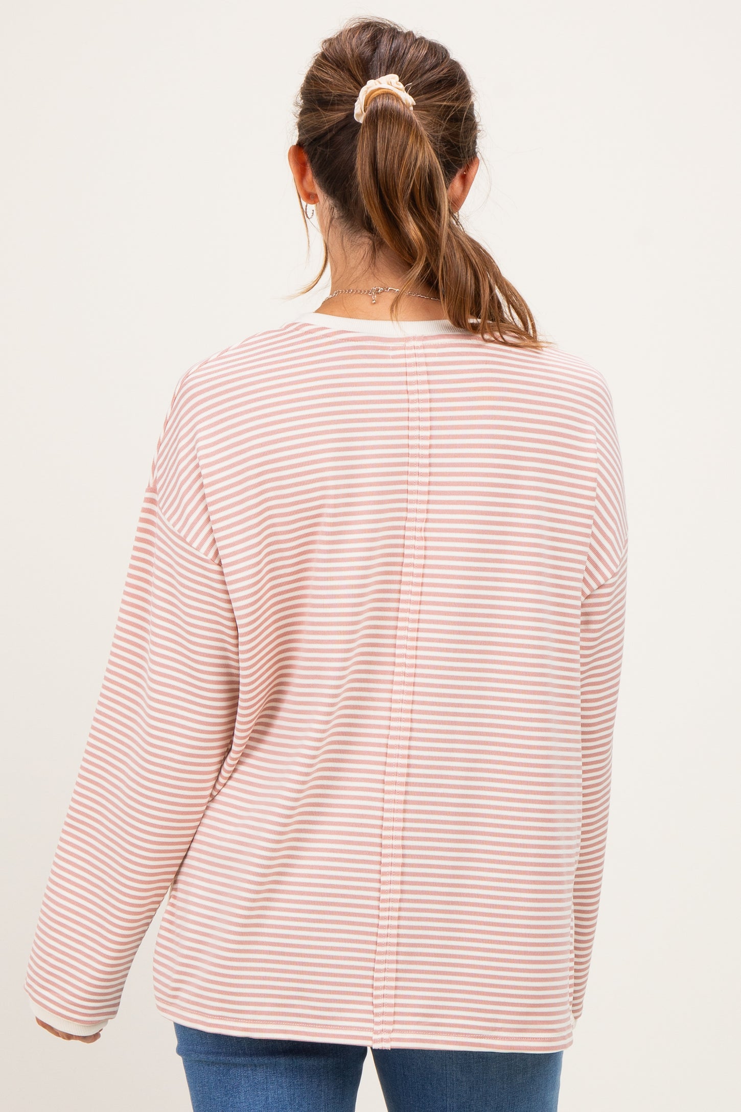 woman wearing a striped maternity top in soft pink and white, viewed from the back