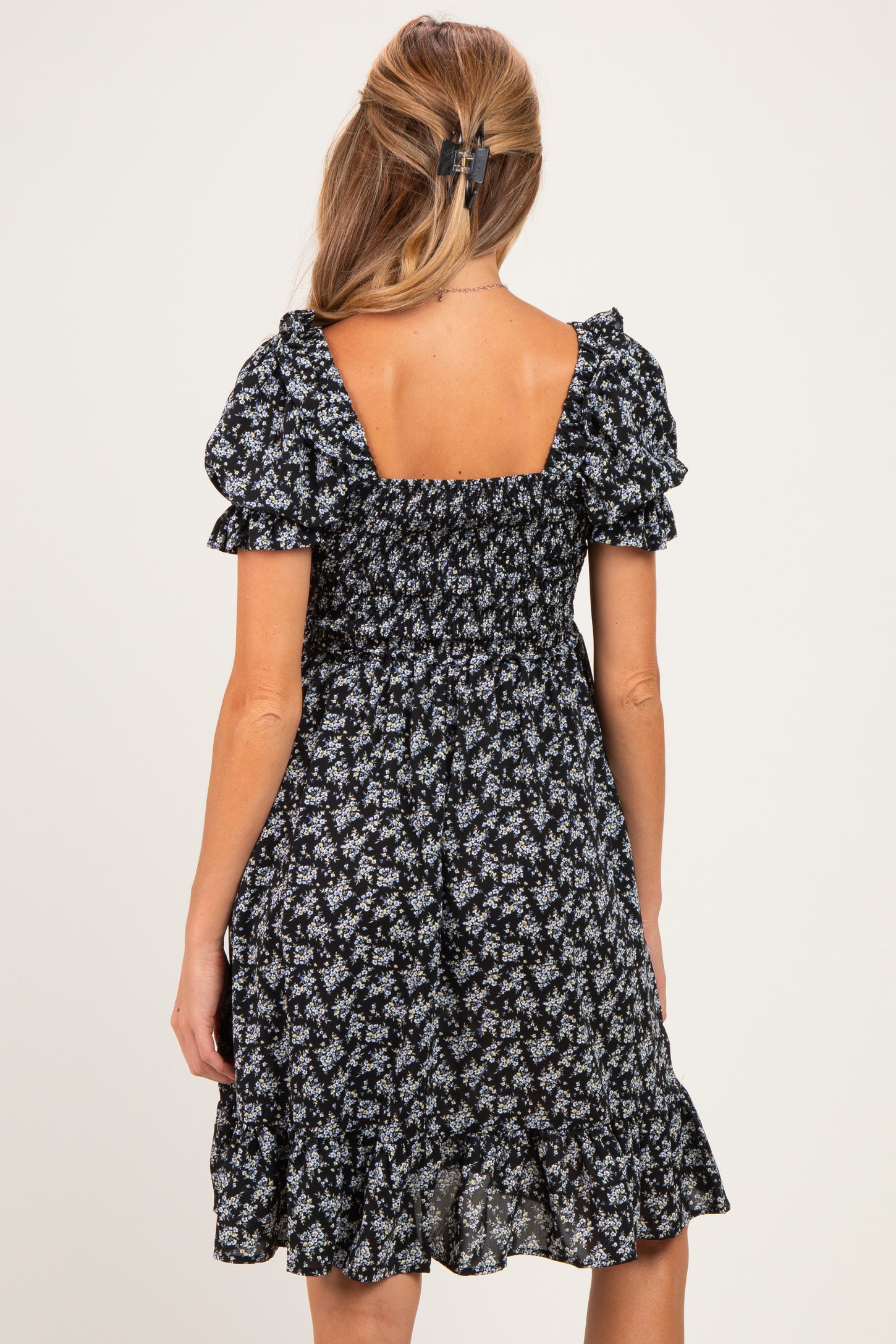 woman wearing a black floral maternity dress with puff sleeves and a tiered skirt
