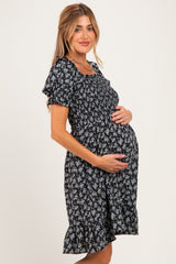 woman wearing a black floral maternity dress with short sleeves and a ruffled hem, showcasing her baby bump