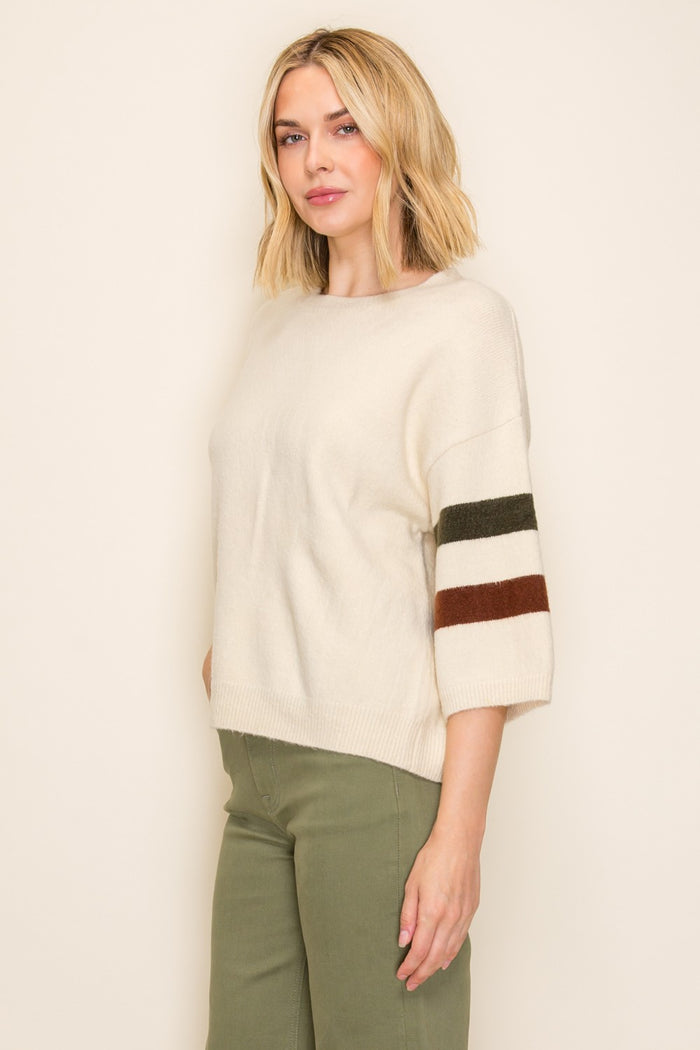 woman wearing an ivory oversized sweater with color block stripes on the sleeves and green trousers