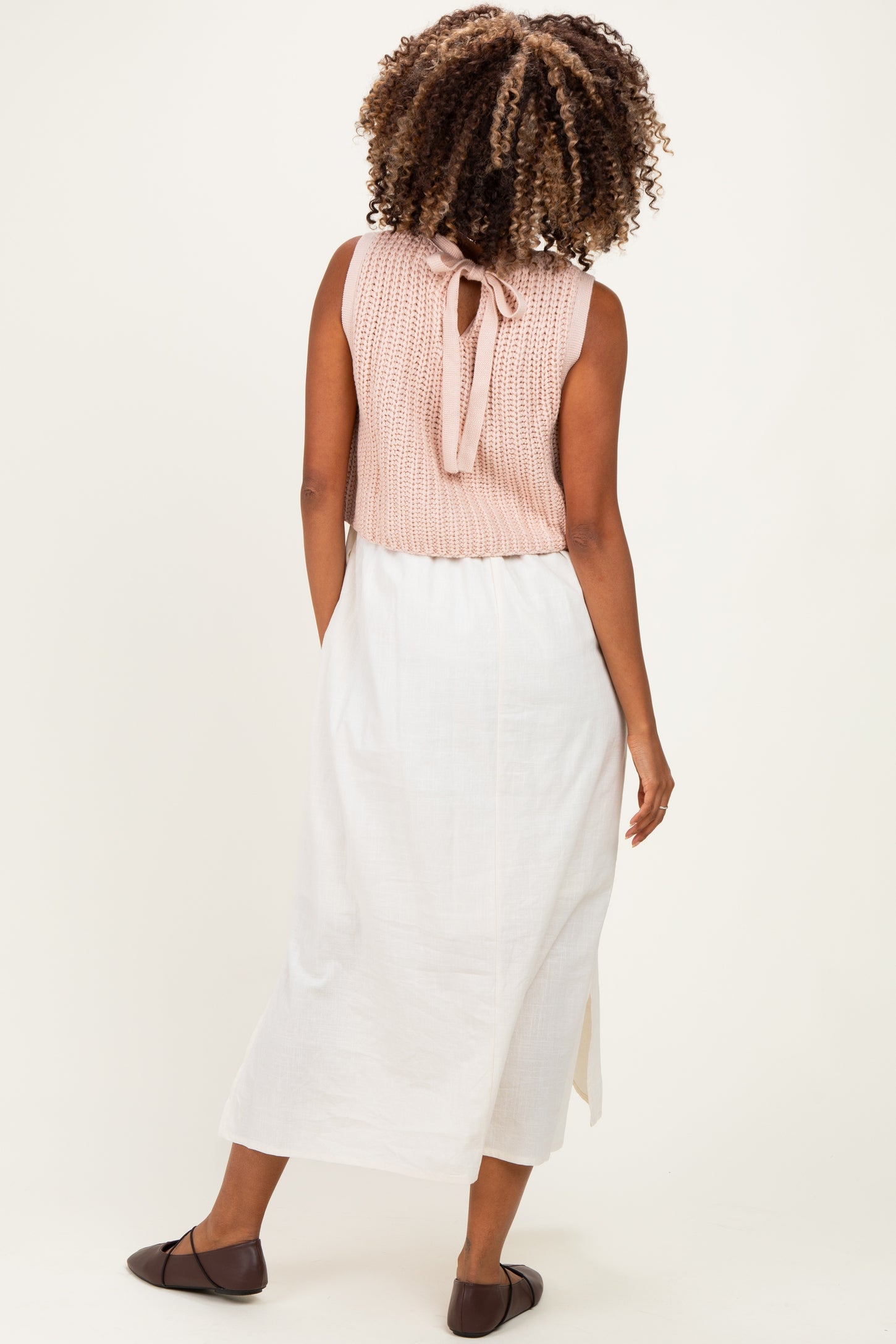 woman wearing a light pink sleeveless maternity top with a back tie, paired with a white maxi skirt