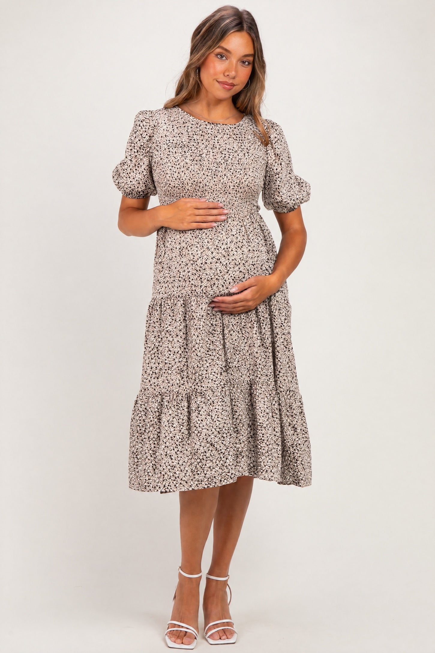 woman wearing a beige floral maternity dress with puff sleeves and tiered skirt, holding her baby bump