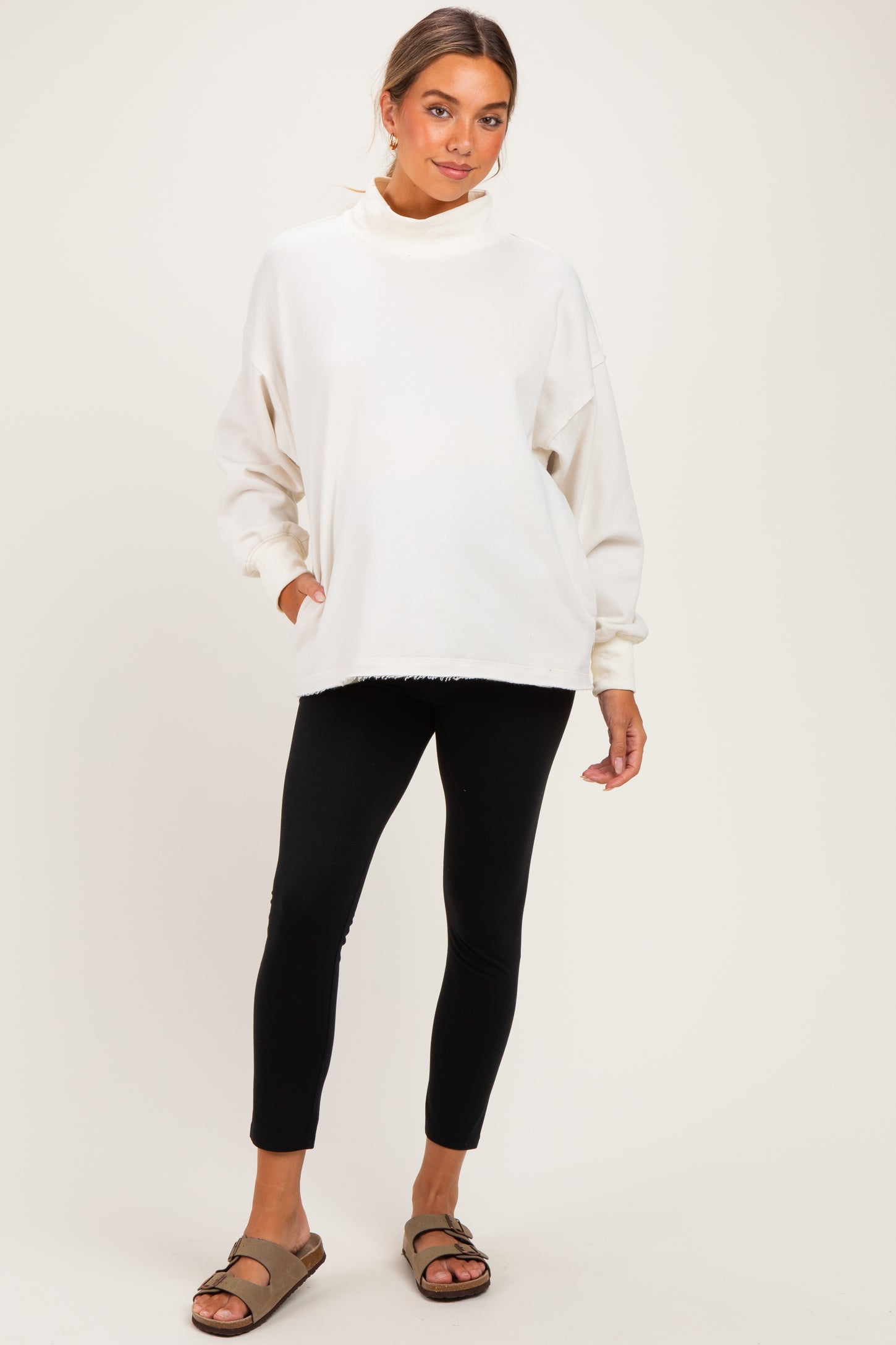 woman wearing a cream oversized maternity sweatshirt with a high neck and black maternity leggings