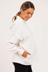woman wearing a cream maternity pullover sweatshirt with pockets, smiling and showing her baby bump
