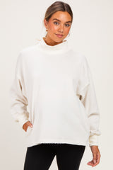woman wearing an oversized cream maternity sweatshirt with a mock neck and long sleeves, paired with black leggings