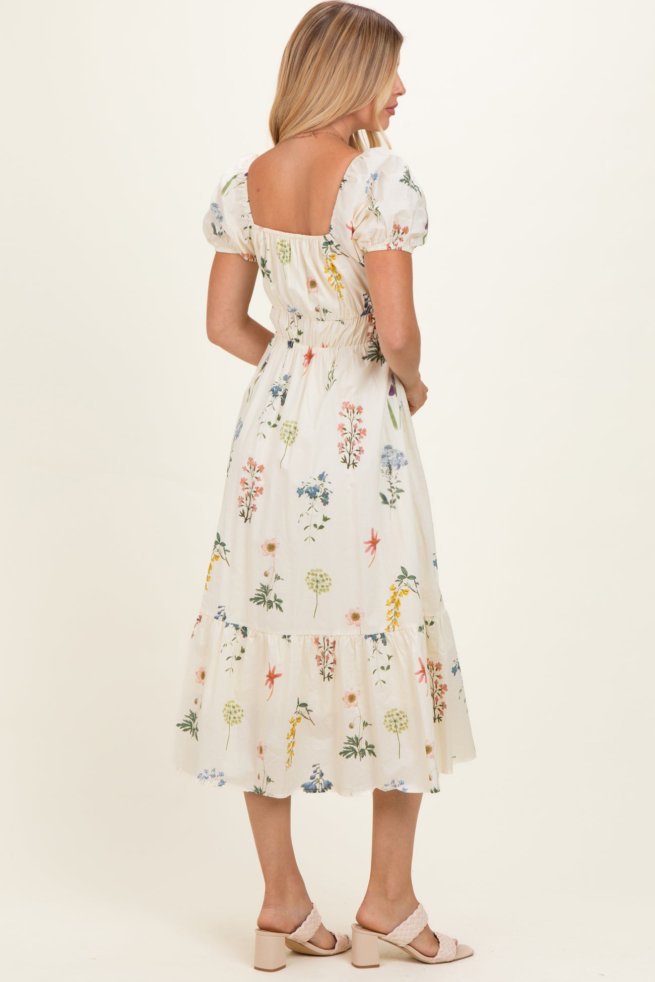 woman wearing a white floral midi dress with puff sleeves and a smocked back, standing with her back to the camera