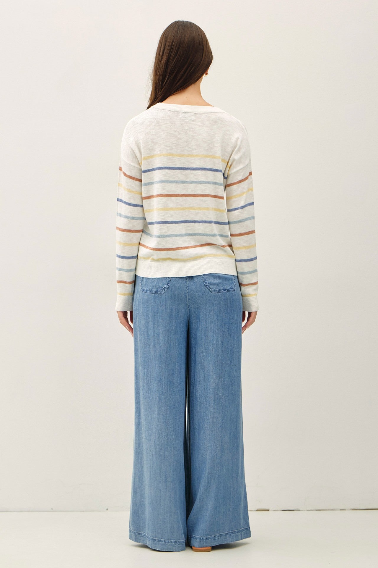 woman wearing a striped sweater in cream and pastel colors with wide-leg denim pants from the back