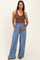 woman wearing a brown ribbed tank top and light blue wide-leg maternity pants, holding her baby bump