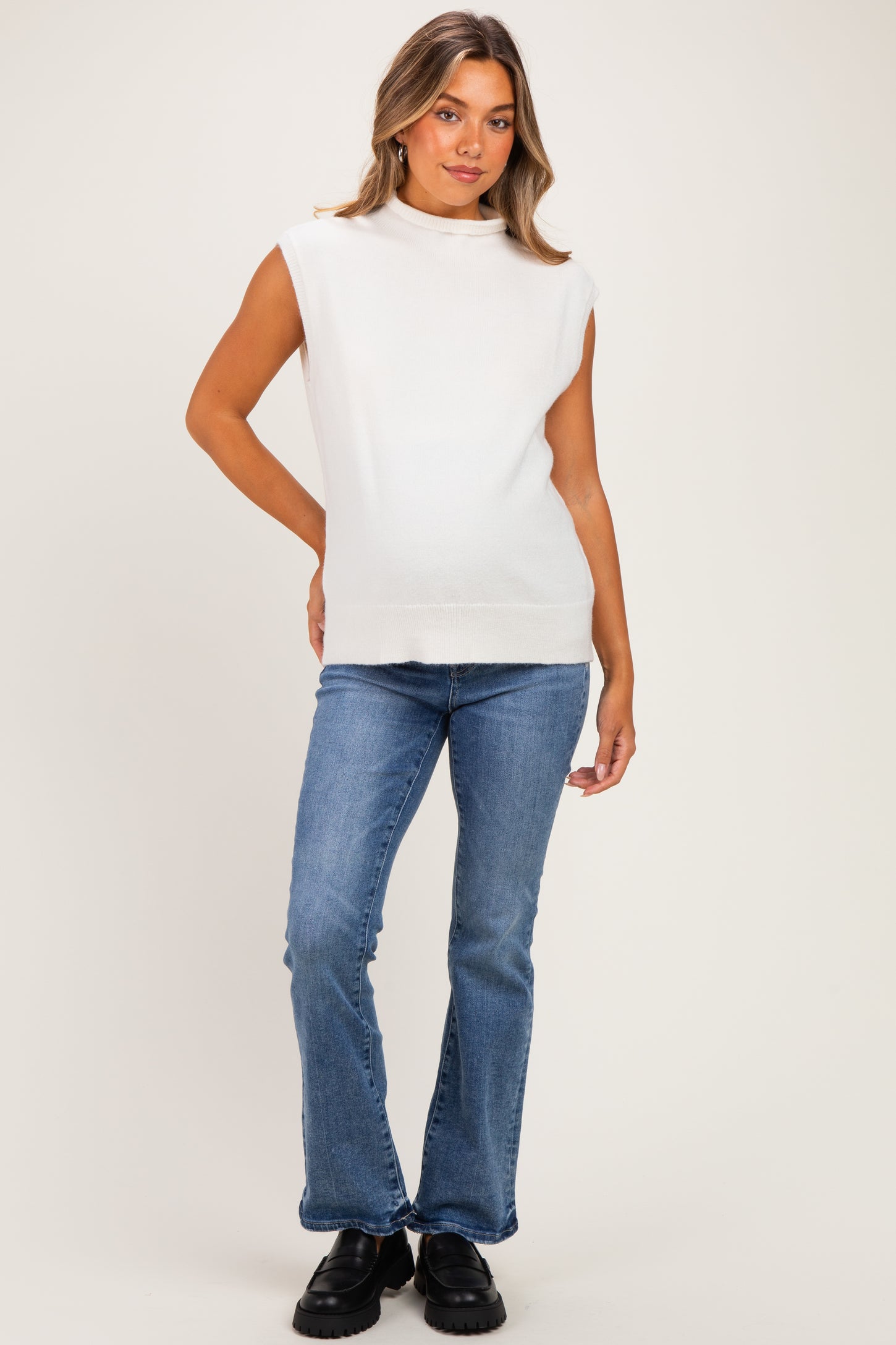 woman wearing a white sleeveless maternity top paired with blue flared jeans