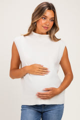 woman wearing a cream sleeveless maternity sweater and gently holding her baby bump