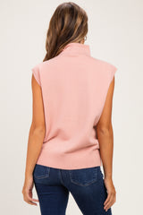 woman wearing a pink sleeveless maternity sweater with a high collar, styled with dark blue jeans
