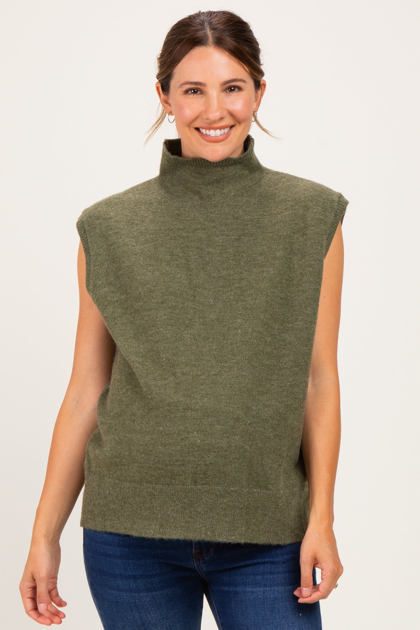 woman wearing a green sleeveless maternity sweater with a mock neck and relaxed fit, smiling against a neutral background