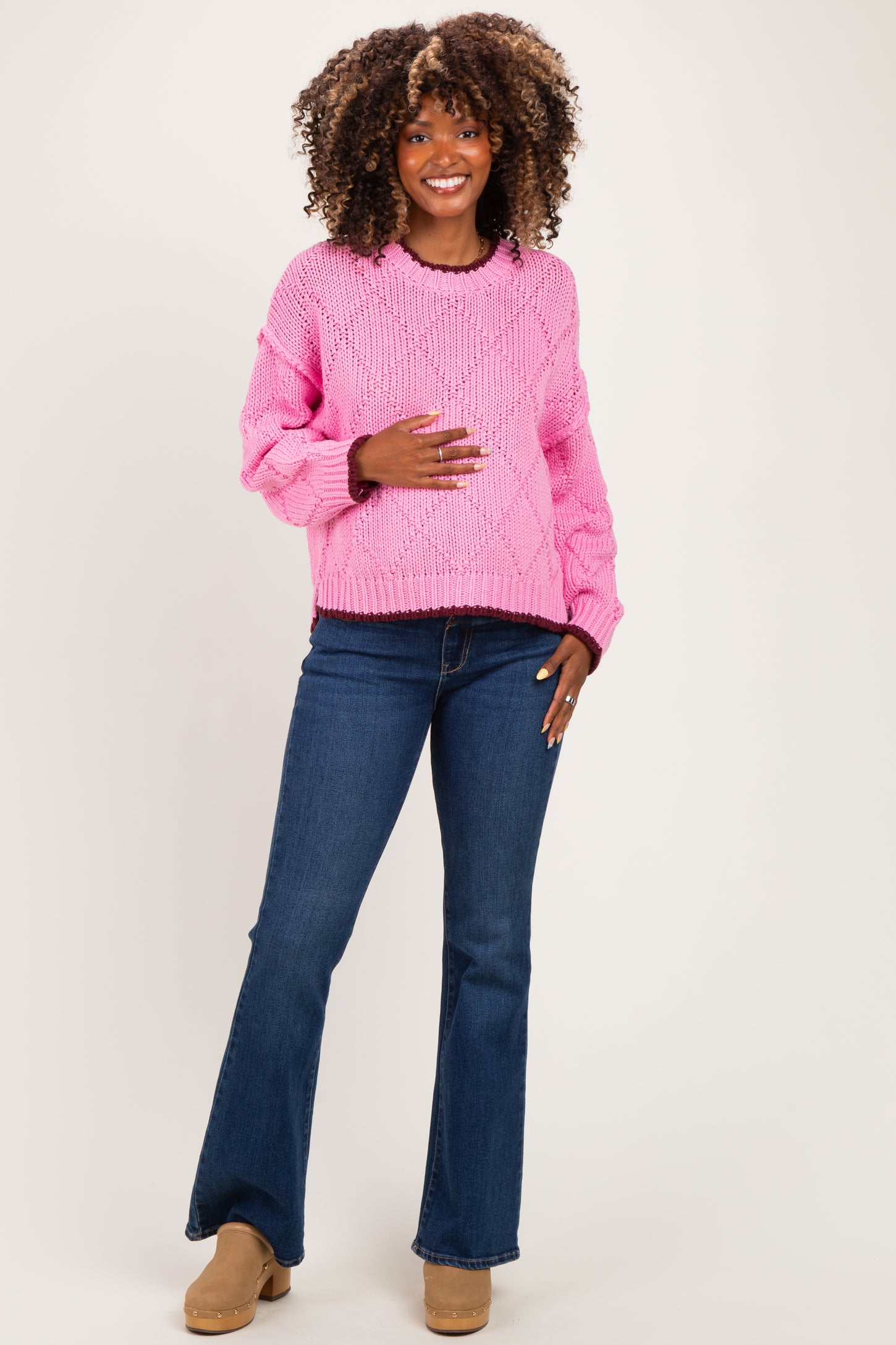 woman wearing a pink knitted maternity sweater and blue flared jeans, holding her baby bump