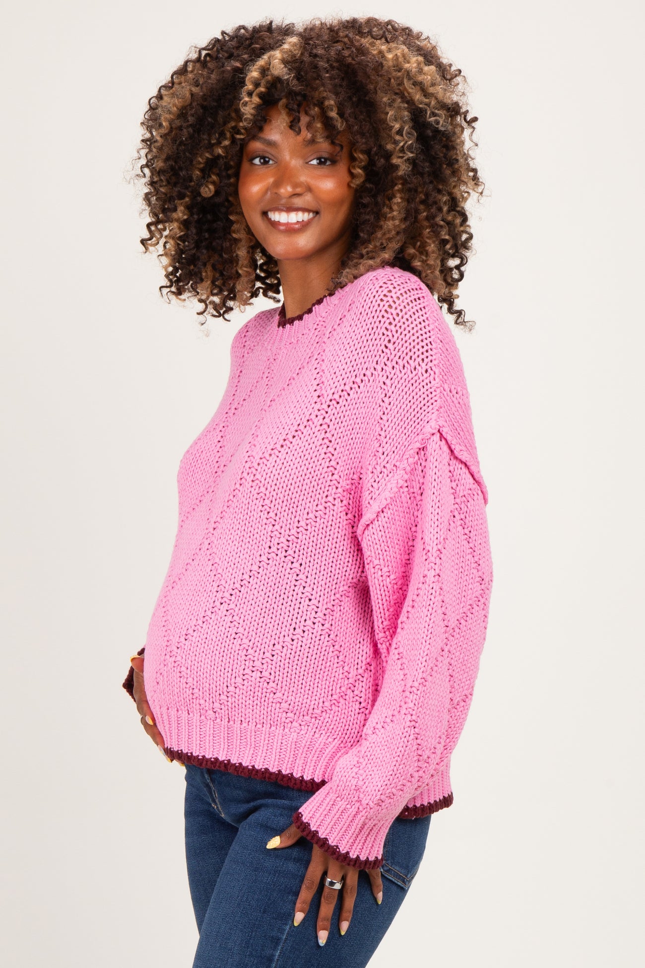 woman wearing a bright pink knitted maternity sweater with a loose fit and a visible baby bump