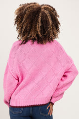 woman wearing a pink oversized maternity sweater with a textured knit design and long sleeves