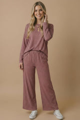 woman wearing a maroon and cream striped long sleeve top and matching wide-leg pants, posing casually