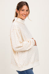 woman wearing a cream floral maternity pullover with a high collar and holding her baby bump