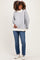 woman wearing a grey floral maternity sweatshirt with a white collar and holding her baby bump, paired with blue jeans