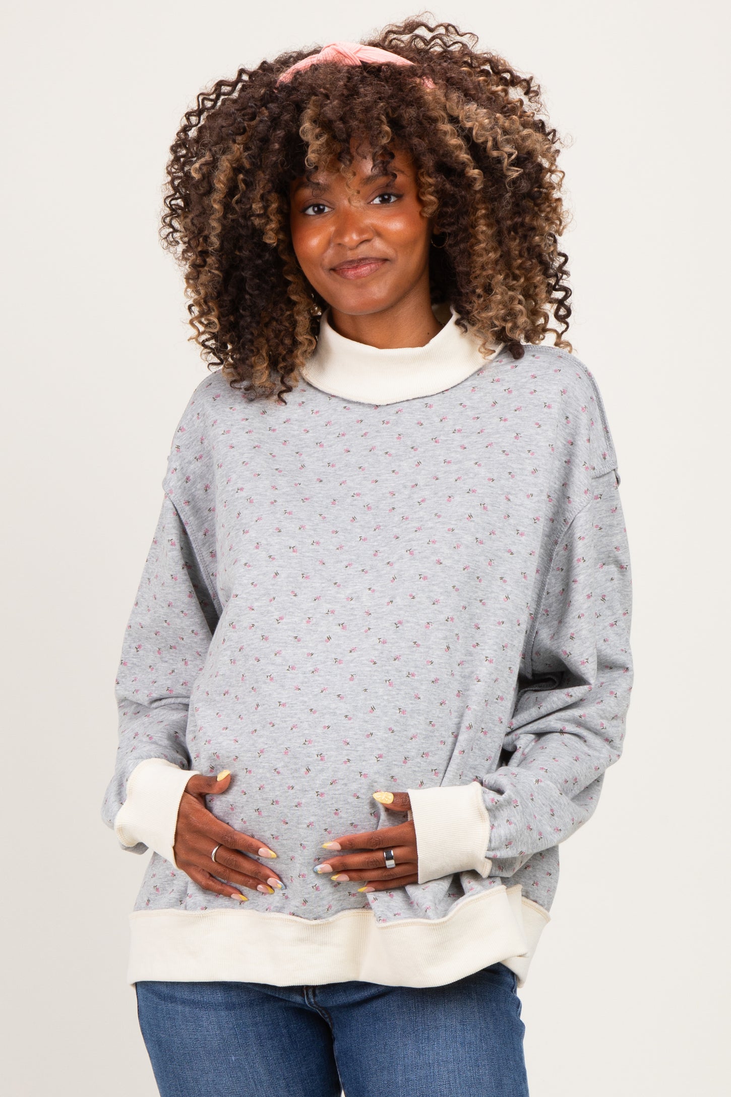 woman wearing a gray floral maternity sweatshirt with a high collar and cream cuffs, gently cradling her baby bump