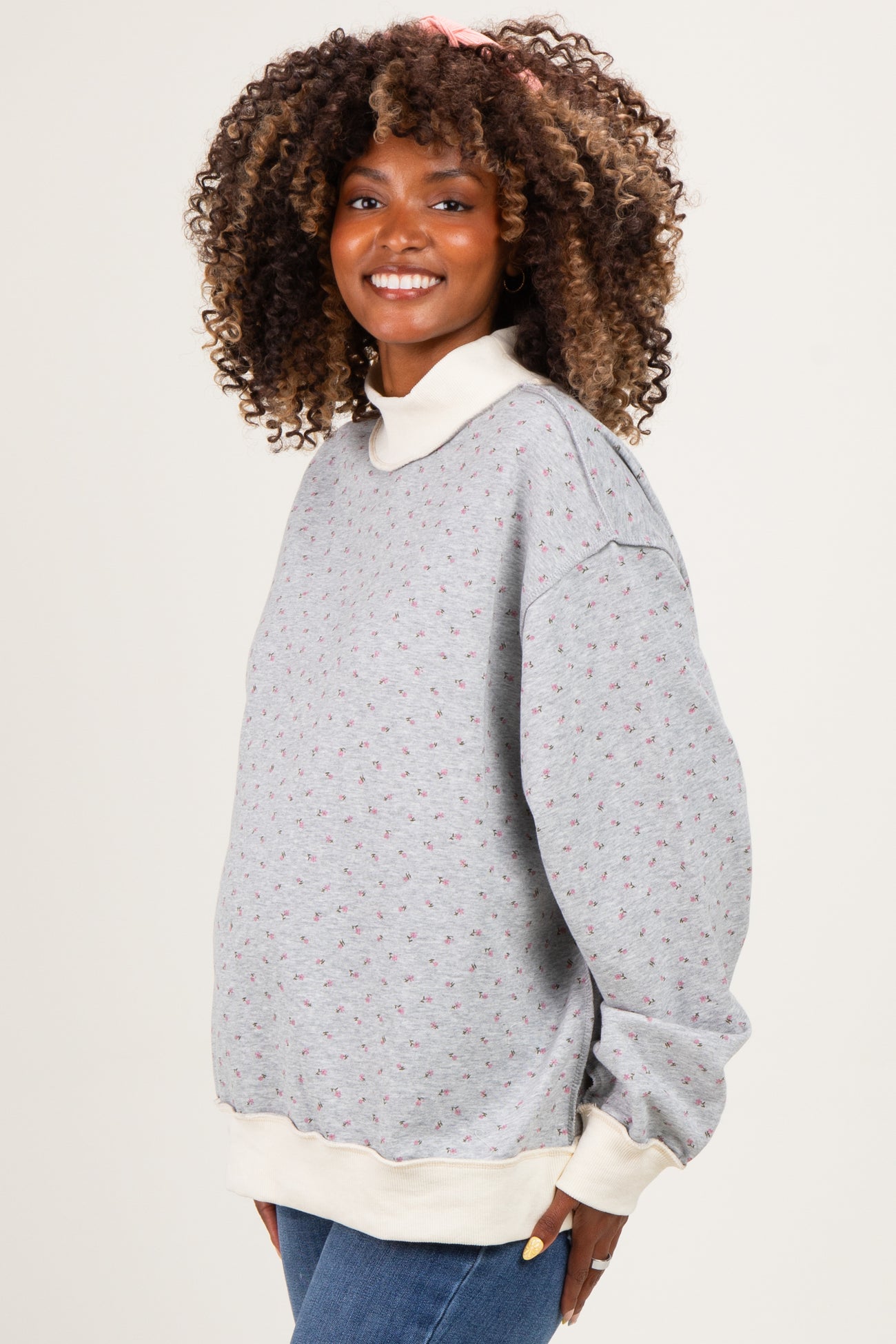 woman wearing a gray floral maternity sweatshirt with a cream collar, showing a visible baby bump, smiling against a neutral background