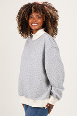 woman wearing a gray floral maternity sweatshirt with a cream collar, showing a visible baby bump, smiling against a neutral background