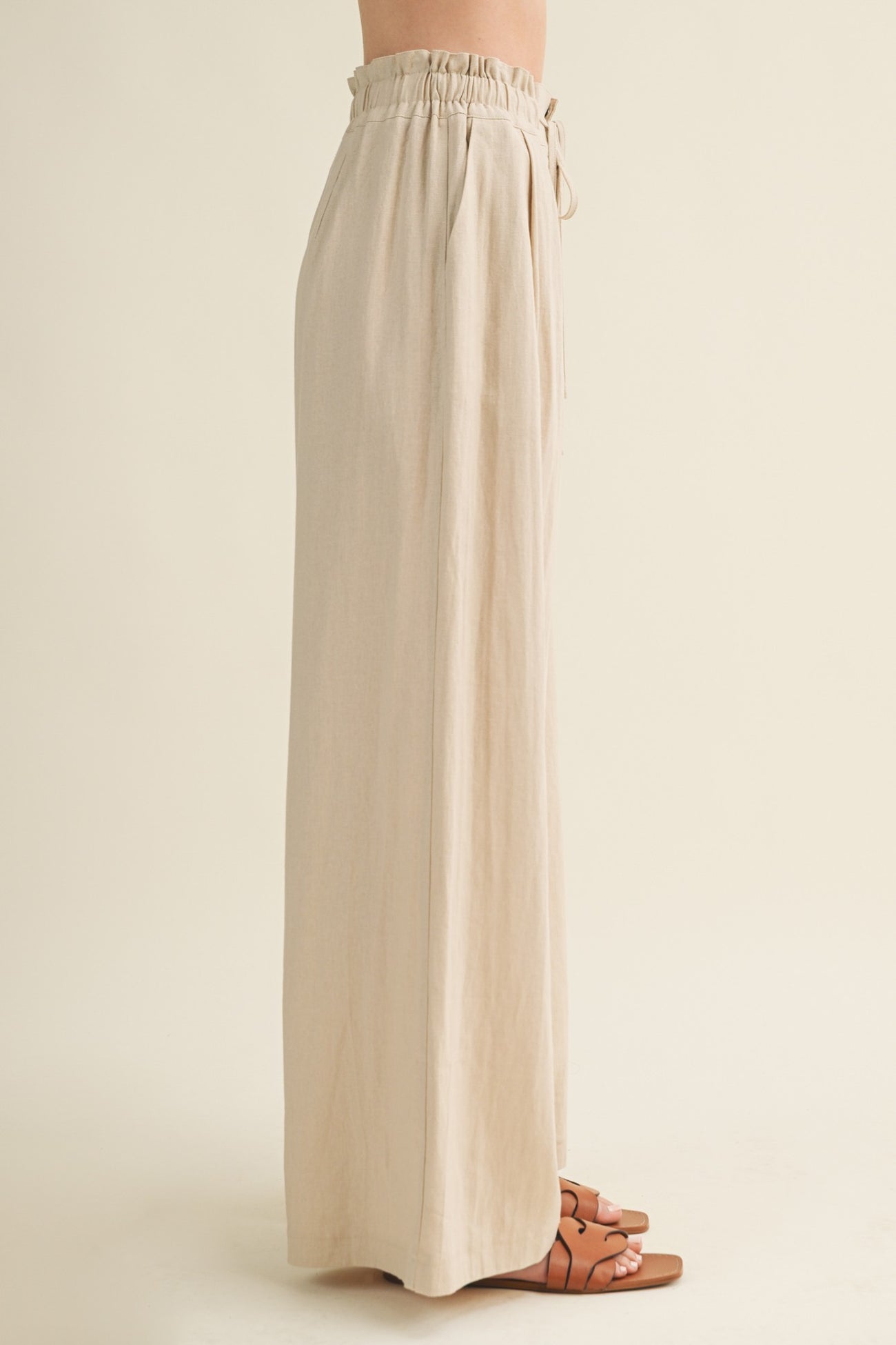 woman wearing high-waisted beige wide-leg trousers with an elastic waistband and drawstring detail