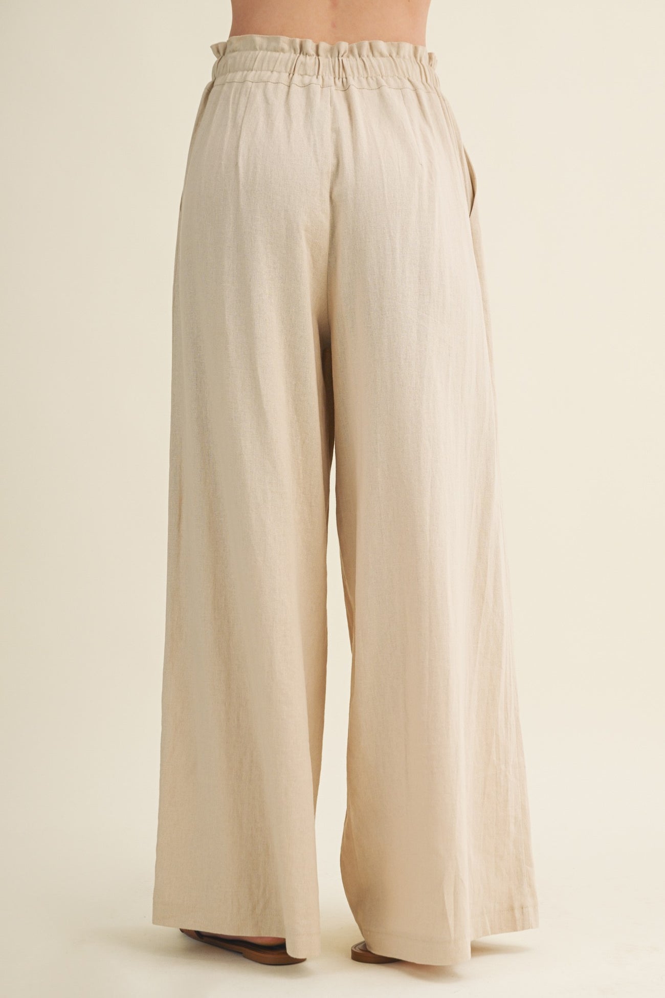 woman wearing light beige wide leg pants with an elastic waistband, viewed from the back