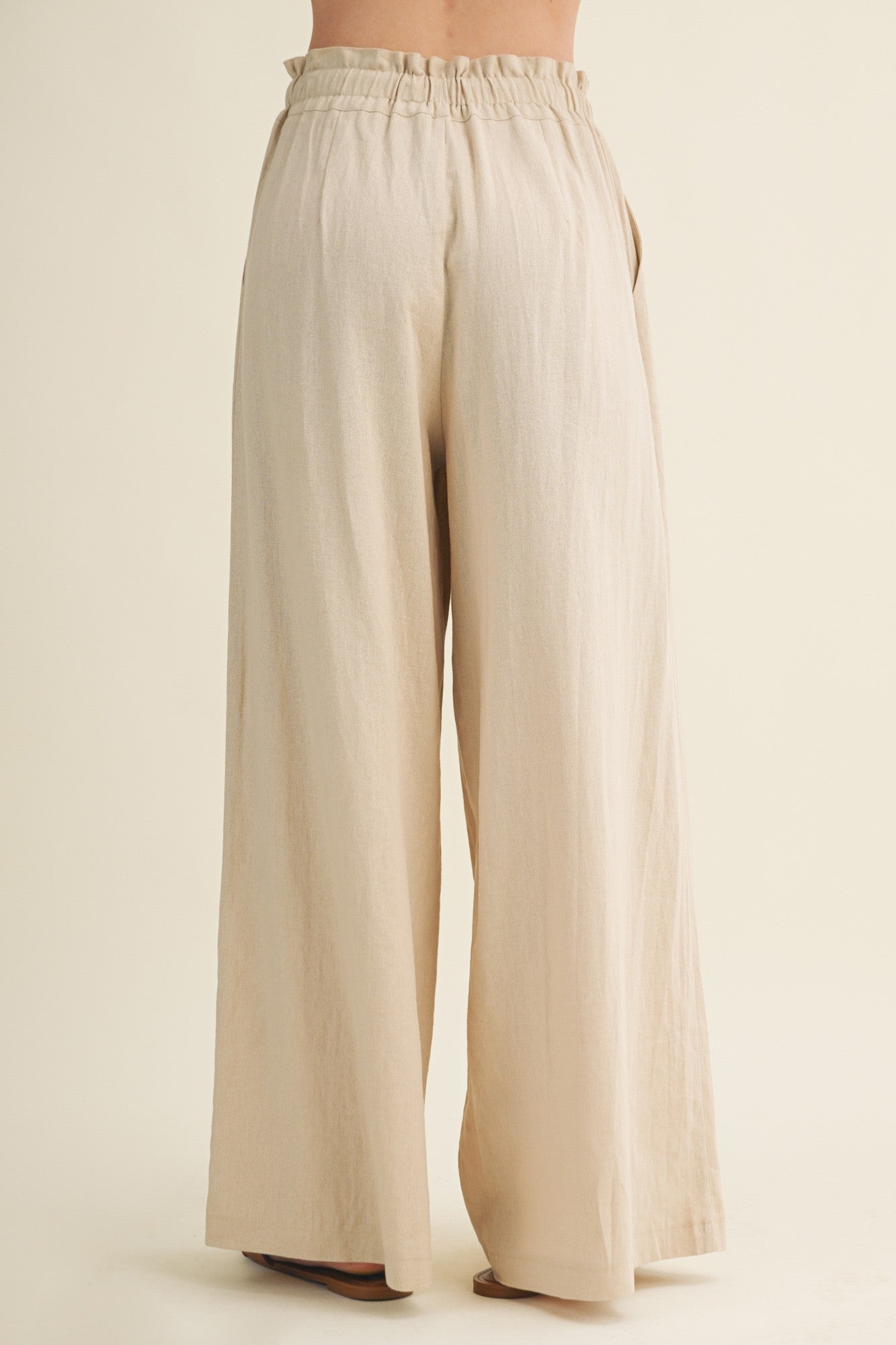woman wearing light beige wide leg pants with an elastic waistband, viewed from the back