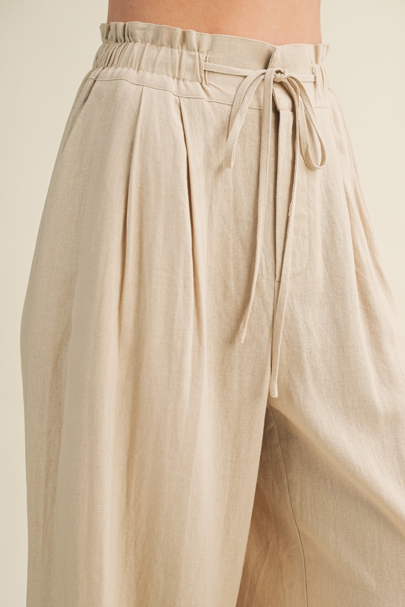 woman wearing beige high-waisted wide-leg pants with a tie waist and pleated details