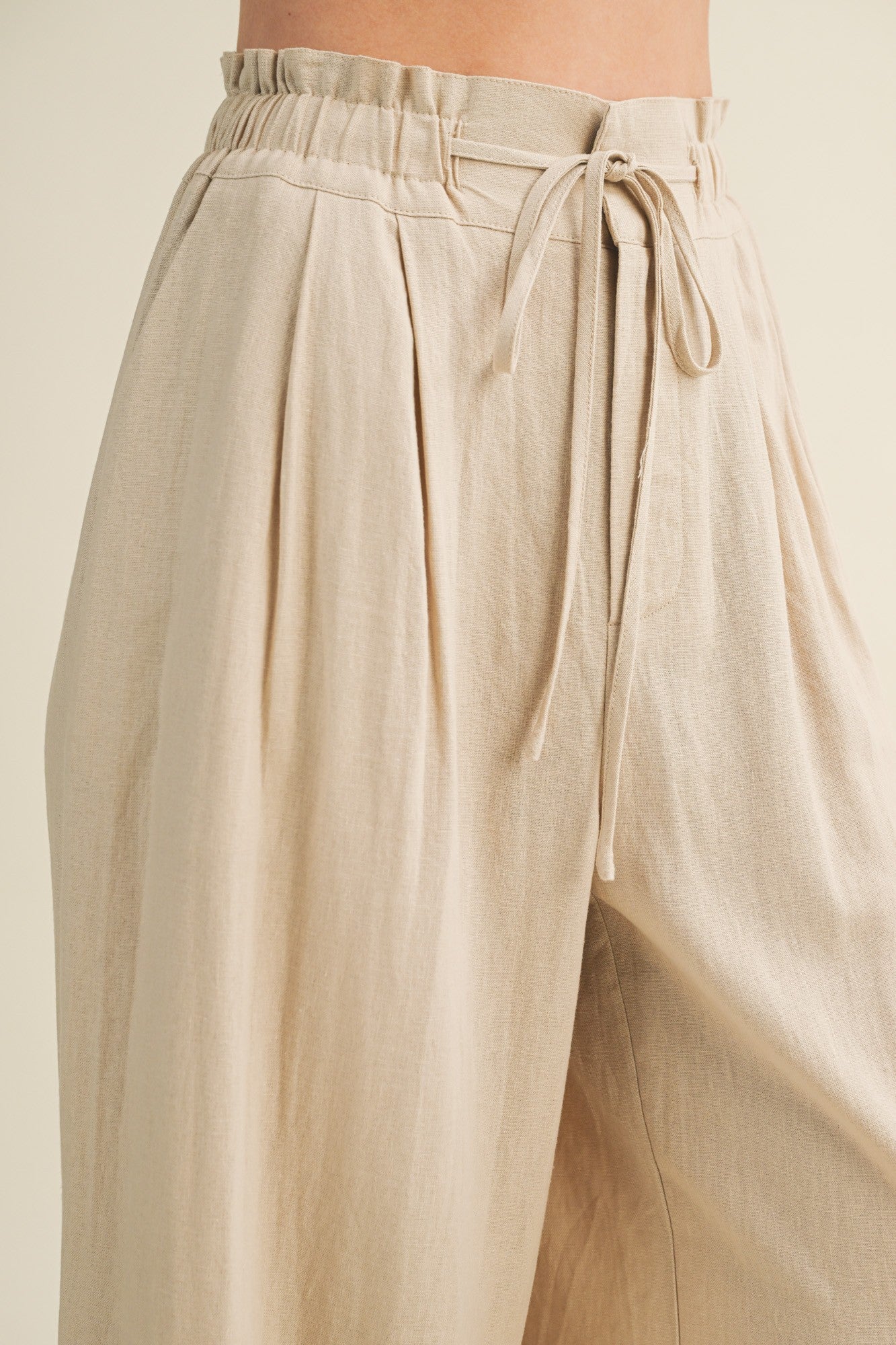 woman wearing beige high-waisted wide-leg pants with a tie waist and pleated details