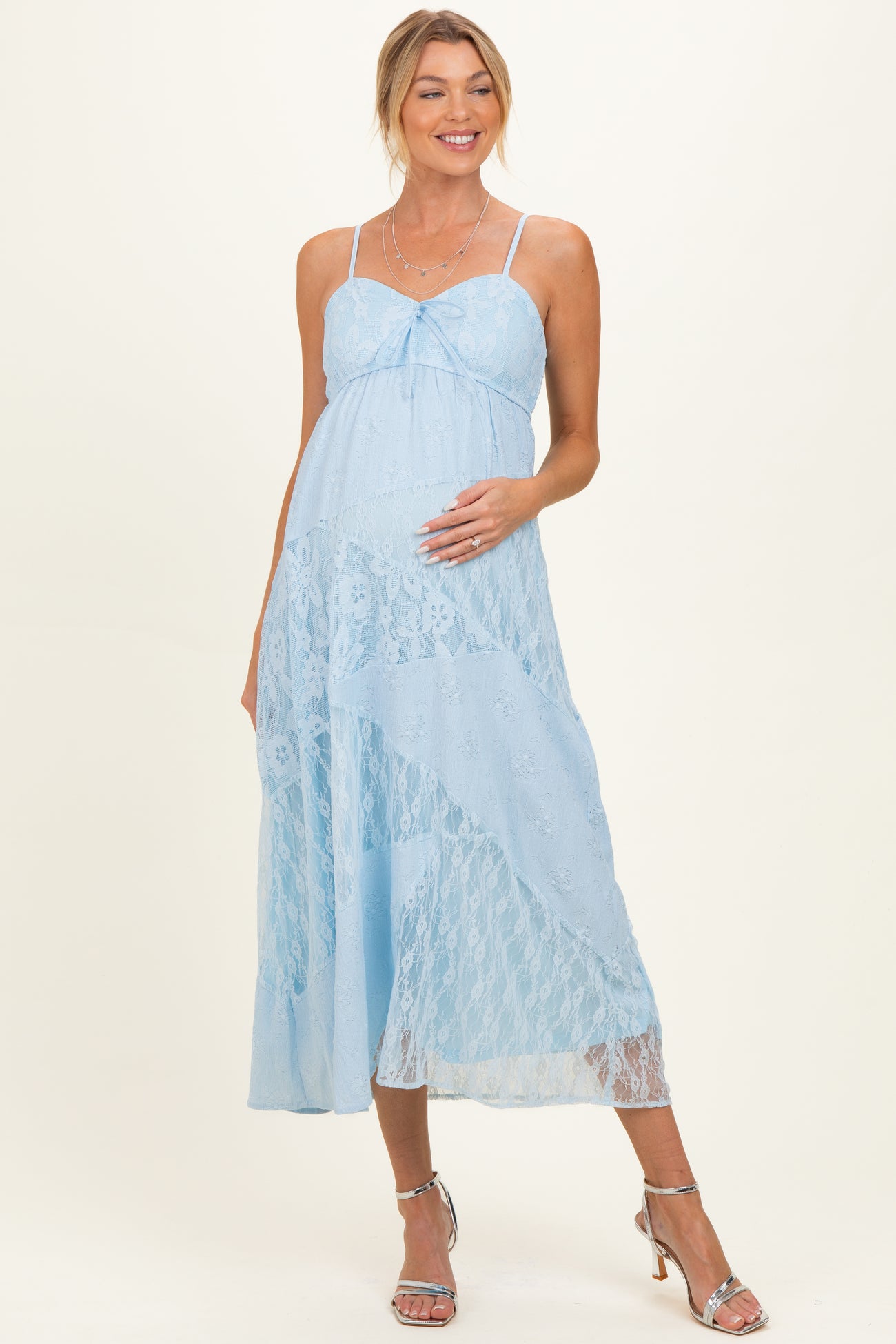 woman wearing a light blue lace maternity dress with adjustable straps and a flowing skirt, holding her baby bump