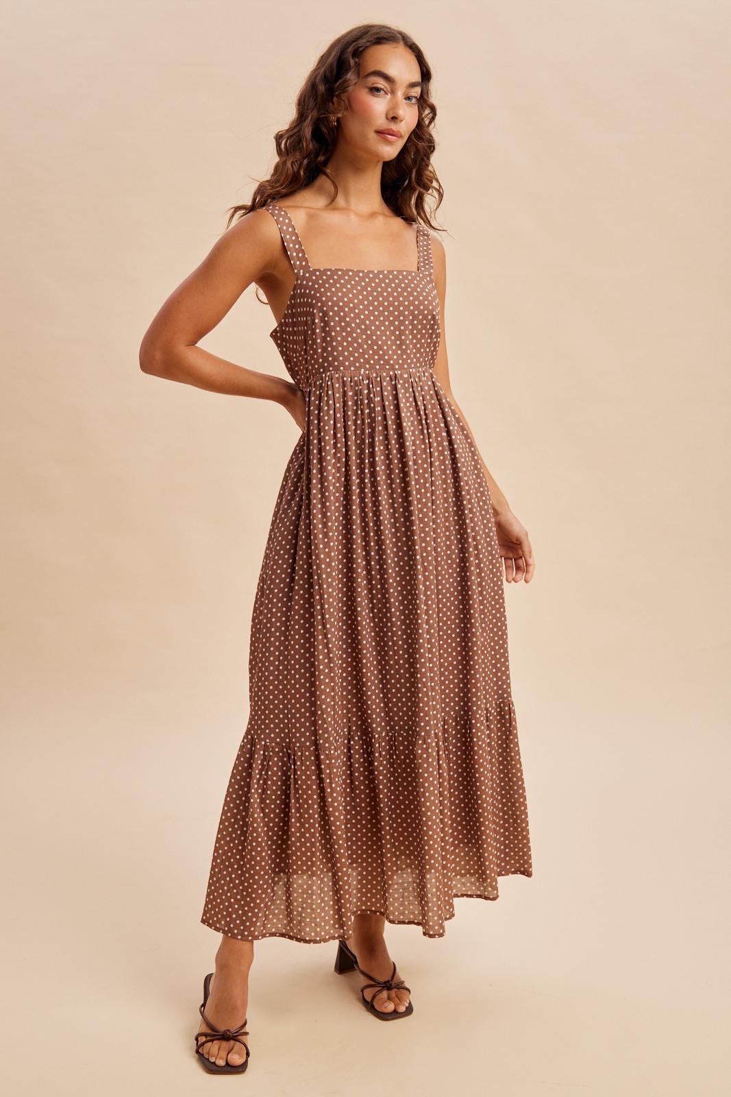 woman wearing a brown polka dot maxi dress with a square neckline and tiered skirt, standing against a neutral background