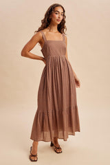 woman wearing a brown polka dot maxi dress with a square neckline and tiered skirt, standing against a neutral background